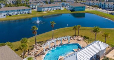 Beautiful resort-style community pool surrounded by palm trees, lounge chairs, and shaded seating. A perfect spot to swim, relax, and enjoy the sunny coastal atmosphere during your stay.
