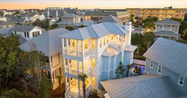 Beautiful coastal home captured at sunset with warm interior lighting, highlighting classic architecture and inviting outdoor spaces.