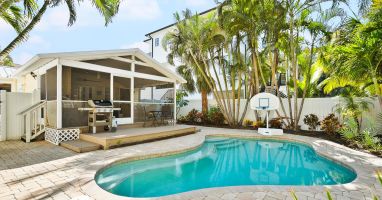 This tropical backyard features a private swimming pool, a built-in grill, and lush palm landscaping—perfect for relaxing outdoor meals after a beach day.
