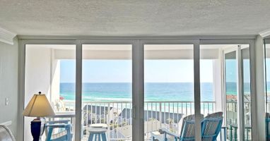 Step into your beachfront haven where floor-to-ceiling windows frame endless ocean views and your private balcony awaits with comfortable seating.