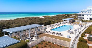 Beachfront property featuring elevated pool deck with pristine white sand beach and turquoise waters beyond natural dune vegetation.