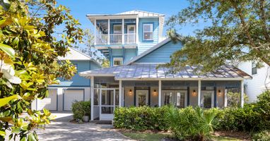 Charming coastal home with distinctive blue siding and metal roof, featuring wraparound porches and mature landscaping in a peaceful setting.