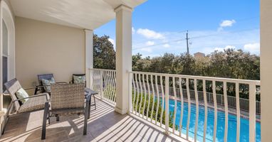 Relax on your private balcony with wicker seating while enjoying stunning pool views and lush surroundings.