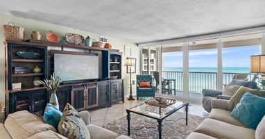 Sink into plush sofas while ocean waves dance beyond your floor-to-ceiling windows in this elegant beachfront living room.