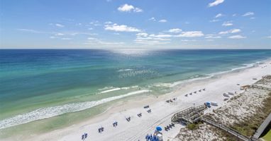 Stunning aerial view of pristine white sand beach with turquoise waters and beachside amenities including umbrellas and boardwalk access.