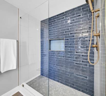 Step into a spa-like shower with stunning blue tile that mirrors the Gulf and sea glass–inspired flooring that brings the beach inside—complete with a handheld sprayer and a sleek glass toe ledge for added comfort.