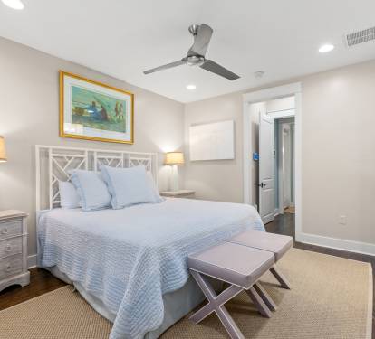 Bright bedroom view w/ cushioned bench, coastal art & a calm, uncluttered layout.