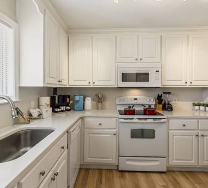 Bright, fully equipped kitchen with white cabinetry, spacious countertops, and modern appliances. Features a large sink, dishwasher, stove, and built-in microwave, with a clean, airy layout perfect for preparing meals and hosting guests comfortably.