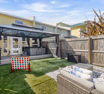 Cozy covered outdoor patio with string lights, a private hot tub, and a gas grill perfect for relaxing evenings and outdoor dining in a fenced backyard space.