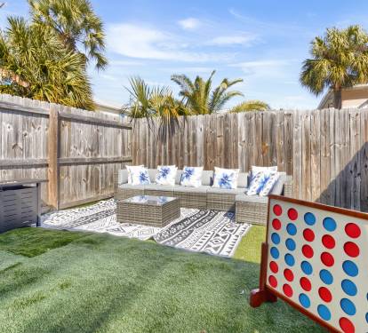 Bright and private backyard hangout area featuring a covered patio with a grill, artificial turf lawn, outdoor lounge seating, and fun games ideal for relaxing, BBQs, and family-friendly entertainment.