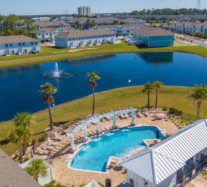 Beautiful resort-style community pool surrounded by palm trees, lounge chairs, and shaded seating. A perfect spot to swim, relax, and enjoy the sunny coastal atmosphere during your stay.