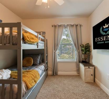 Fun and cozy bunk bedroom perfect for kids or groups, featuring comfortable beds, soft linens, and a wall-mounted TV. Bright natural light and thoughtful d&eacute;cor make this space ideal for relaxing after a day of adventure.