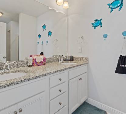 Bright, clean bathroom with a spacious double vanity, granite countertops, and large mirror. Coastal-inspired d&eacute;cor adds a fun touch, with plenty of space for guests to get ready comfortably.