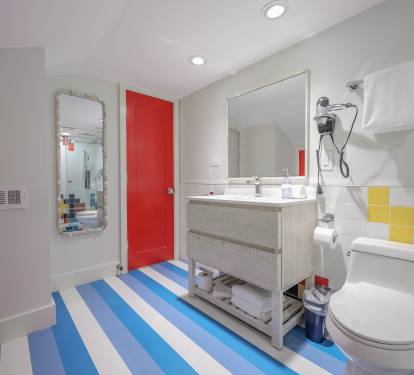 Bright primary bath featuring a walk-in shower and colorful geometric tile plus the home&rsquo;s signature blue-and-white striped flooring.