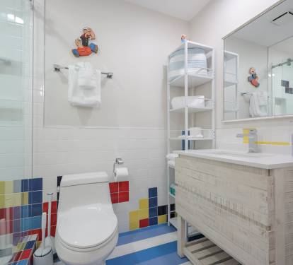 Convenient downstairs full bath with modern walk-in shower, vibrant tile accents, and signature blue-and-white striped flooring.