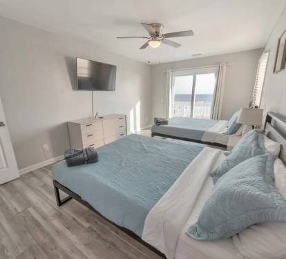 Bright bedroom with two full beds, dresser, and mounted TV.