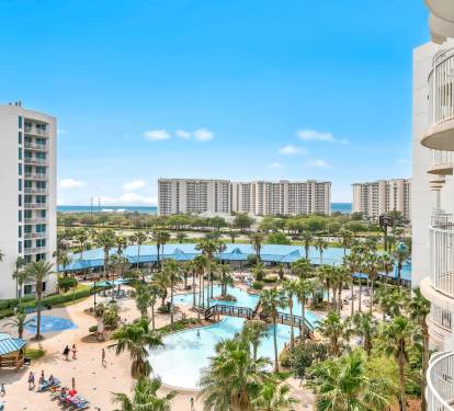 Elevated view overlooking palm-filled resort pools & tropical grounds below