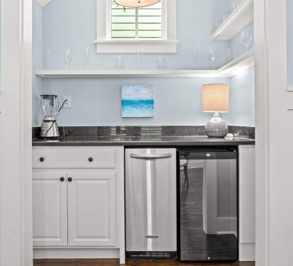 Compact beverage station w/ granite counter, sink & glass-front fridge for easy snacks and drinks.