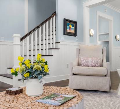Cozy corner of the living room w/ plush armchair, soft lighting & staircase detail that adds charm and warmth.