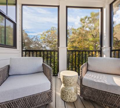 A cozy seating area on the same screened porch offers a quiet spot for morning coffee or evening conversation. Comfortable lounge chairs and a side table create an inviting retreat just steps from the dining space.
