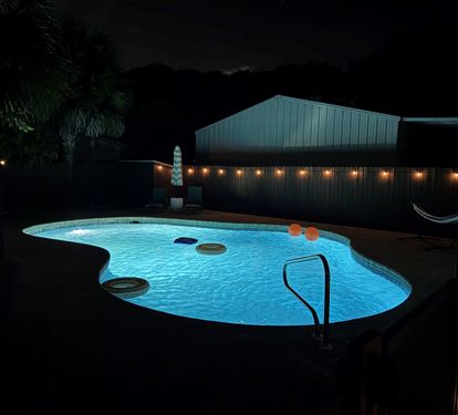 Swim after dark. The pool glows blue with underwater lighting while string lights flicker overhead, turning your backyard into the best bar in PCB.