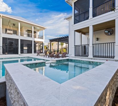 Step into the raised spa and watch it spill straight into the pool below — hot tub and pool working together, with both homes framing the scene behind you.
