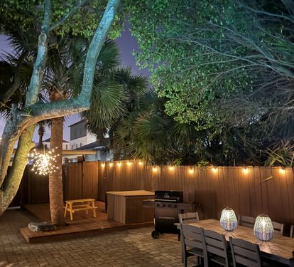 After dark, the backyard comes alive. Brick pavers glow under lanterns, the dining table is set for late-night bites, and the lit pool beckons beyond the gas grill.