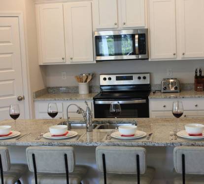 Bright full kitchen with counter seating for 4, a stove, microwave, sink, and 2-door fridge.
