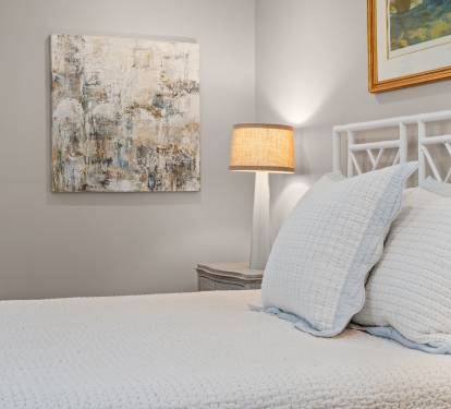 Serene bedroom detail w/ textured bedding, soft artwork & warm bedside lighting for restful evenings.