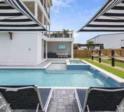 Spacious outdoor area featuring a large pool, hot tub, loungers, hammock, and umbrellas.

