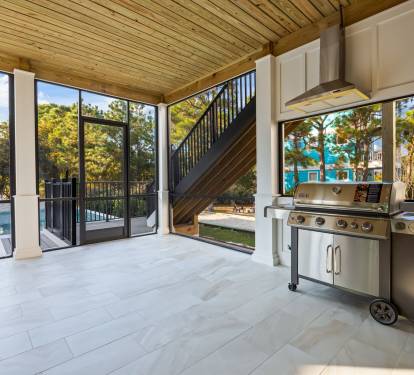 Covered outdoor kitchen and dining patio just off the main living area, featuring a gas grill with permanent propane hookup—no tanks to change or worry about—and open views toward the pool. Fully screened for comfort with wall-mounted fans, this inviting 