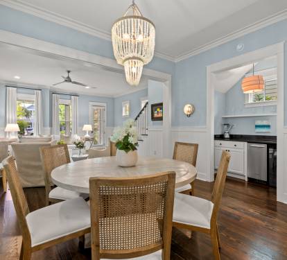 Open dining area w/ round table, woven chairs & elegant chandelier, flowing seamlessly into the living space.