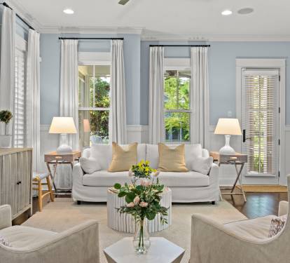 Airy living room w/ cozy sofa, layered lighting & garden views through tall windows.