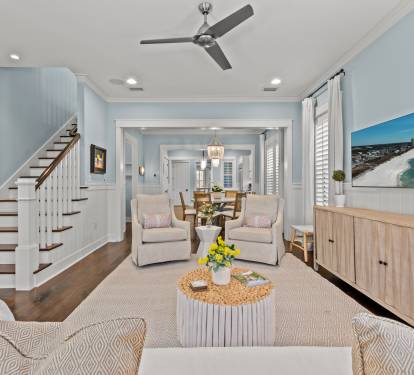 Wide view of the living room w/ cozy seating, ceiling fan & an open flow into the dining area.