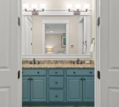 Double-sink vanity w/ granite counters, blue cabinetry & clean, modern lighting.