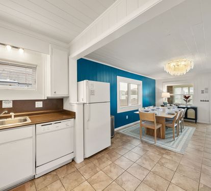 The open-plan kitchen and dining area flow together so the cook is never cut off from the conversation. White cabinets, full appliances, and a clear sight line to the table.