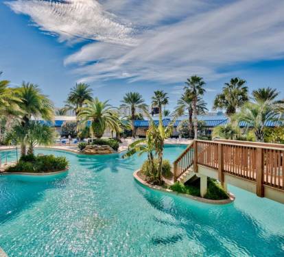 Resort-style pool w/ winding waterways, palm trees, and a sunny bridge connecting lush islands.