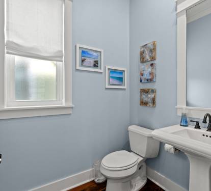 Clean half bath w/ pedestal sink, coastal art & soft blue walls for a fresh feel.