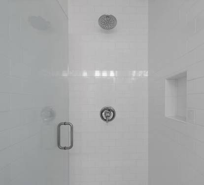 Tiled-in shower with frameless glass shower door and rainfall shower head.