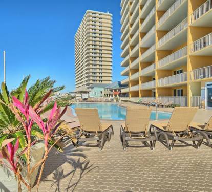 A hotel pool area with lounge chairs and a large building in the background.