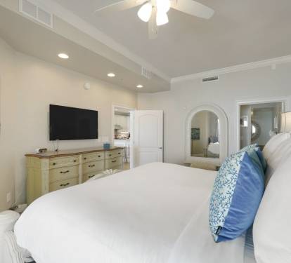 This spacious bedroom features a ceiling fan, flat screen TV, elegant furnishings, with soaker tub/walk-in shower, and sliding glass doors that open to stunning Gulf views