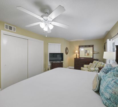 Bright coastal master suite with plush king bed, flat screen tv, ceiling fan, ample storage, and private retreat atmosphere.