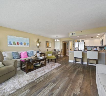 Cabana Club 101 offers a living room that embodies beachside relaxation with two sleeper sofas, natural light pouring through corner windows, and sweeping views of Destin-s Gulf waters
