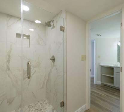 Luxury walk-in shower with marble-look tile and pebble flooring, perfect for relaxing after a day on the beaches of Destin.