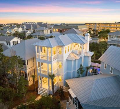 Beautiful coastal home captured at sunset with warm interior lighting, highlighting classic architecture and inviting outdoor spaces.