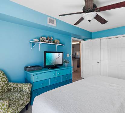 Bright coastal bedroom with pops of color, comfy seating, and a flat-screen TV for easy relaxation.