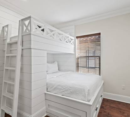 This thoughtfully designed bunk room features a custom-built sleeping area with a full bed below and an upper bunk accessed by a sturdy ladder.