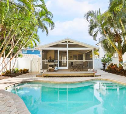 This tropical backyard features a private swimming pool, a built-in grill, and lush palm landscaping—perfect for relaxing outdoor meals after a beach day.