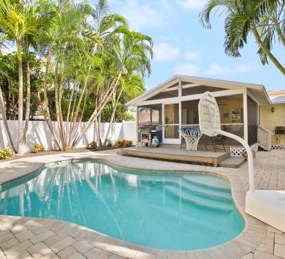 This tropical backyard features a private swimming pool, a built-in grill, and lush palm landscaping—perfect for relaxing outdoor meals after a beach day.