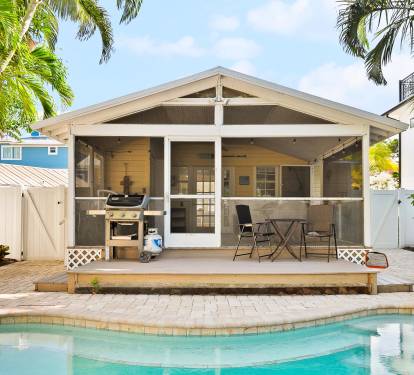 This tropical backyard features a private swimming pool, a built-in grill, and lush palm landscaping—perfect for relaxing outdoor meals after a beach day.
